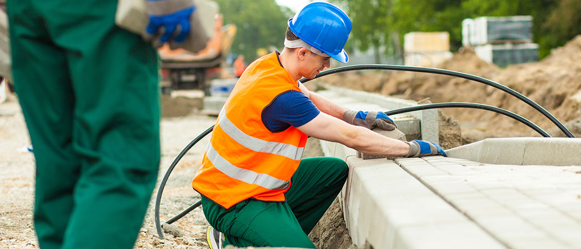 Brickworker kneeling to lay bricks on road side Brickworker kneeling to lay bricks on road side